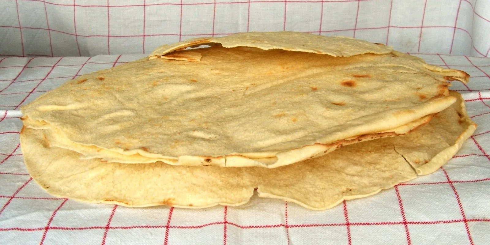 Fogli di pane carasau sardo appoggiati su una tovaglia a quadretti bianchi e rossi