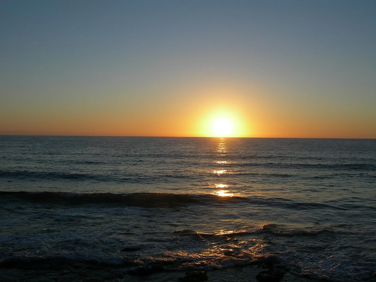 Il sole che tramonta sull'orizzonte del mare a Bosa, con le onde illuminate dalla luce arancione